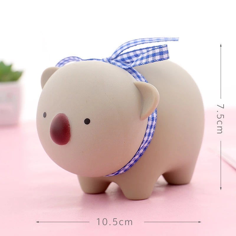 Ceramic piggy bank with a blue checkered ribbon on a pink surface, with measurements indicated.