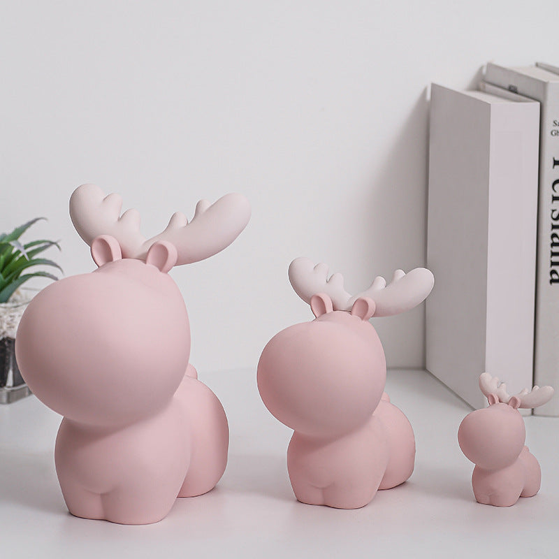 Three pink moose figurines on a light surface with books and a plant in the background. Piggy Bank.