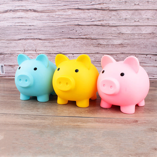 Three colorful piggy banks (blue, yellow, pink) on a wooden surface.
