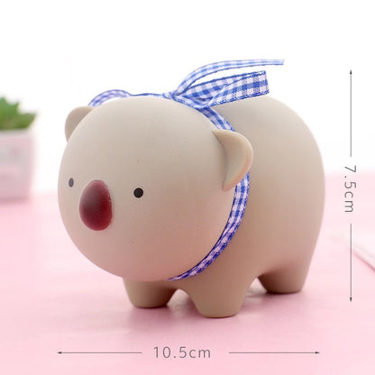 Ceramic piggy bank with a blue checkered ribbon on a pink surface, with measurements indicated.